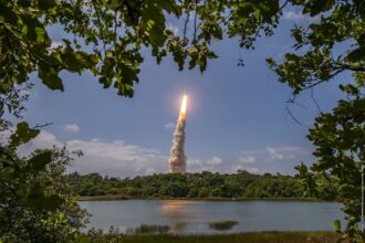 Ariane 6 rocket lifting off from Europe's Spaceport in French Guiana, seen through trees across a lake