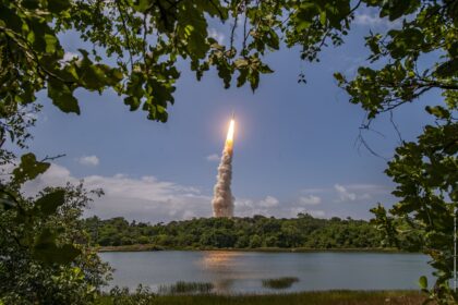Ariane 6 rocket lifting off from Europe's Spaceport in French Guiana, seen through trees across a lake