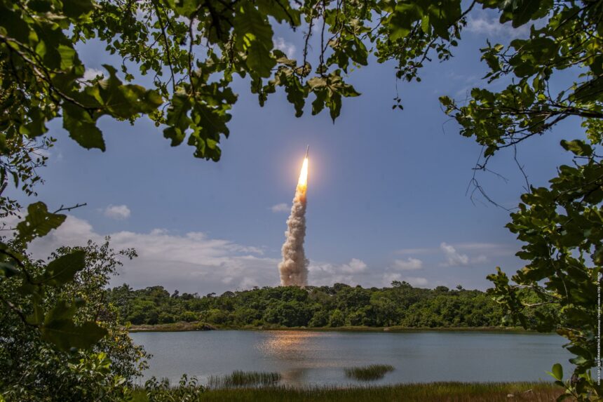 Ariane 6 rocket lifting off from Europe's Spaceport in French Guiana, seen through trees across a lake